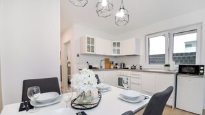 A modern kitchen with white cabinets, a dining area with a table set for two, and a microwave on the countertop. - Stil und Komfort Terrasse - Parkplatz (Bielefeld)