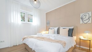 A modern bedroom with a large bed, white bedding, a bedside table with a lamp, and artwork on the walls. - Stil und Komfort Terrasse - Parkplatz (Bielefeld)