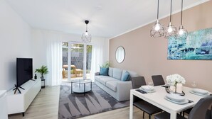 A modern living room with a sofa, dining table, and TV. There is a large window with curtains, a ceiling fan, and a painting on the wall. - Stil und Komfort Terrasse - Parkplatz (Bielefeld)