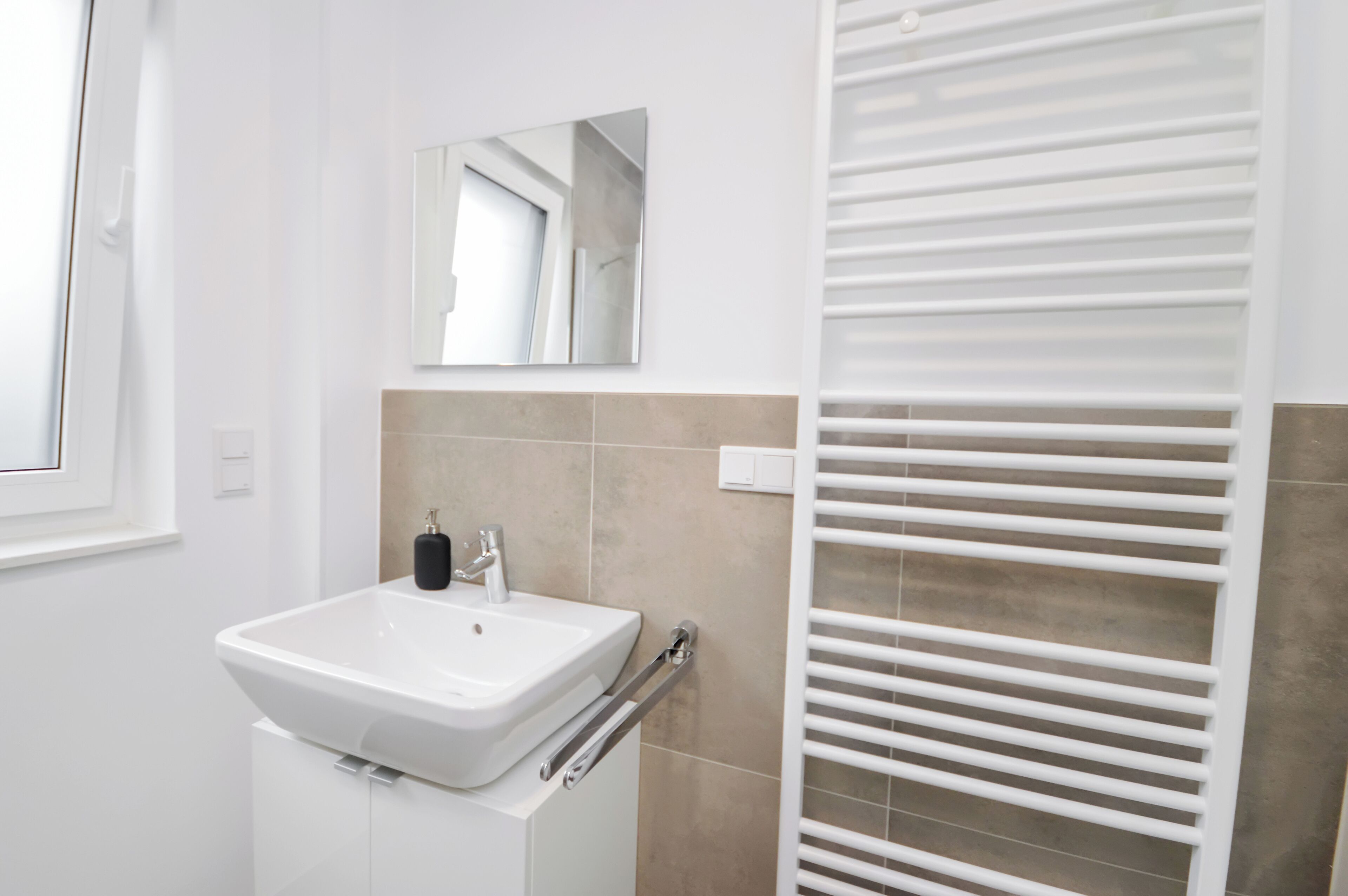 Un baño con un lavamanos blanco, un espejo y un perchero para toallas.