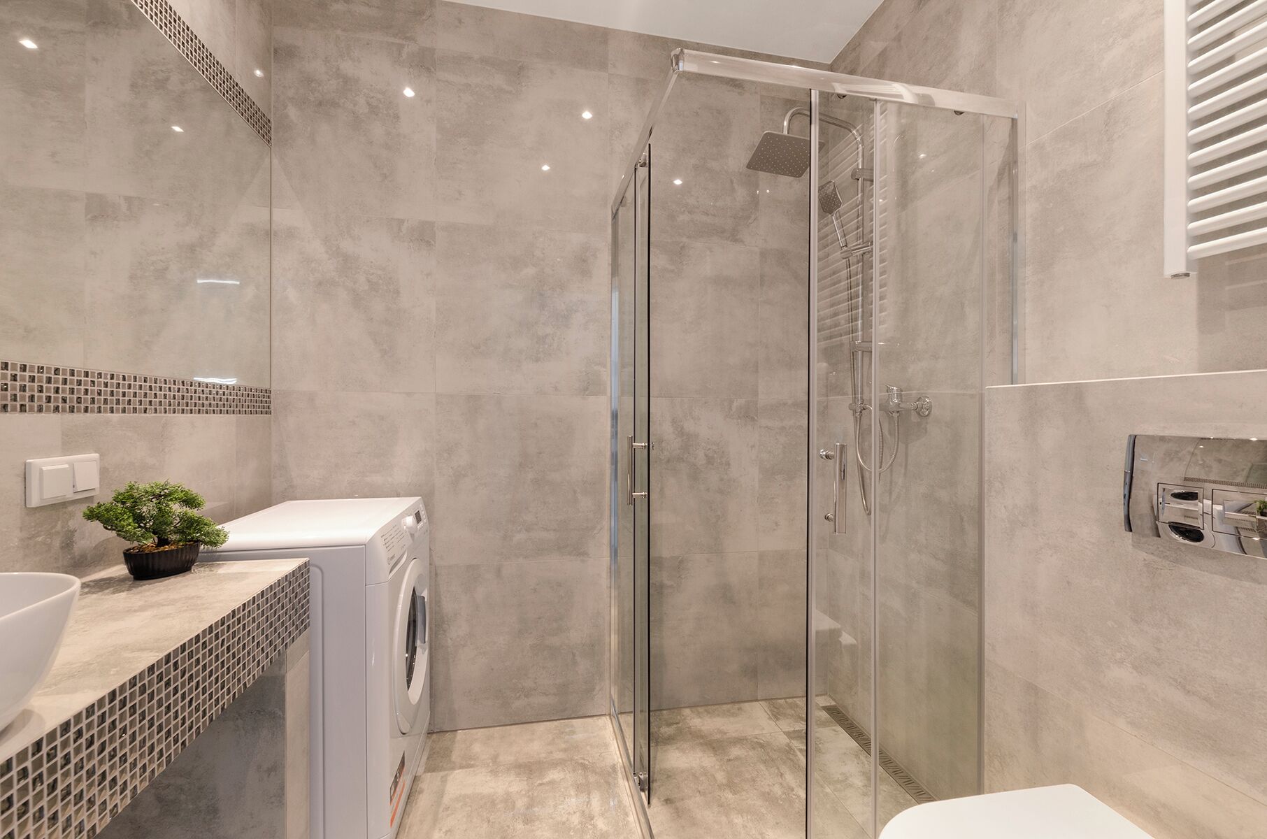 Een moderne badkamer met een glazen douchecabine, een wasmachine en een wastafel met een mozaïek achterwand.