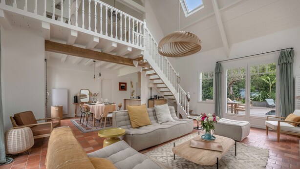 Un salon spacieux avec un plafond haut, un escalier et une grande fenêtre donnant sur l’extérieur.