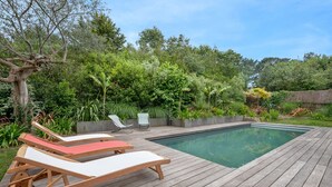 Une terrasse en bois avec une piscine, entourée d’une végétation luxuriante et surmontée d’une structure à toit de chaume.