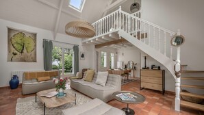 Un salon spacieux avec un haut plafond, un escalier et une grande fenêtre.