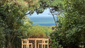 Une table et des chaises en bois, installées dans un jardin avec vue sur la mer.