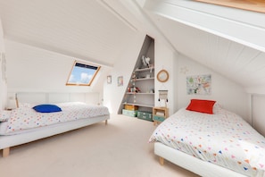 Une chambre avec deux lits, un plafond en pente et un puits de lumière.