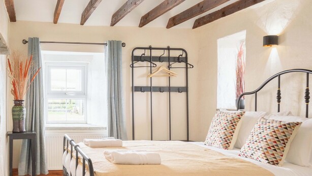 Un dormitorio con cama, ventana con cortinas, radiador y techo de madera.