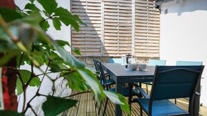 An outdoor patio with a wooden table and chairs, a white wall, and a wooden fence.