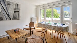 A dining area with a table set for four, surrounded by wicker chairs, a radiator, and a large abstract painting on the wall.