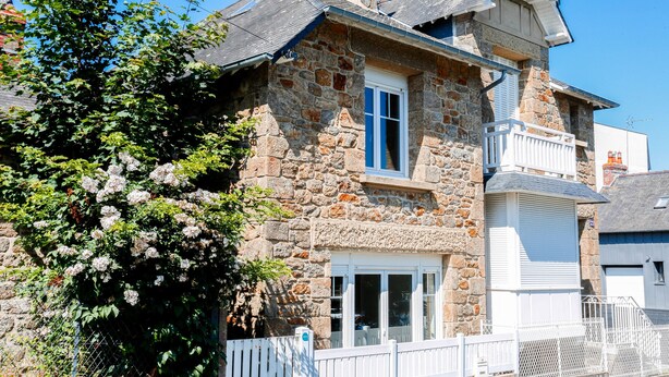A stone house with a balcony, a white fence, and a tree with flowers.