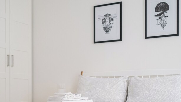A modern bedroom with a neatly made bed, a bedside table with magazines, and two framed artworks on the wall. - Bright and Comfortable Studio Flat, Way Central! (Bologna)