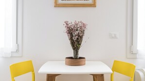 A dining area with a white table, two yellow chairs, a vase of flowers, and a framed painting on the wall. - Bright and Comfortable Studio Flat, Way Central! (Bologna)
