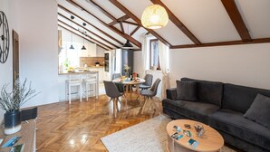 Un'ampia zona giorno con un divano scuro, pavimento in legno e un tavolo da pranzo con sedie.