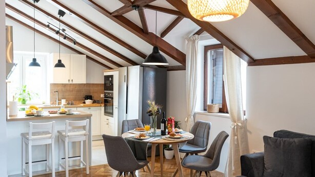 Una cucina moderna con travi in legno, un'area pranzo con tavolo e sedie, e un divano.