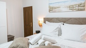 Una camera da letto con un letto, una porta di legno, un comodino, una lampada e un quadro raffigurante una spiaggia.