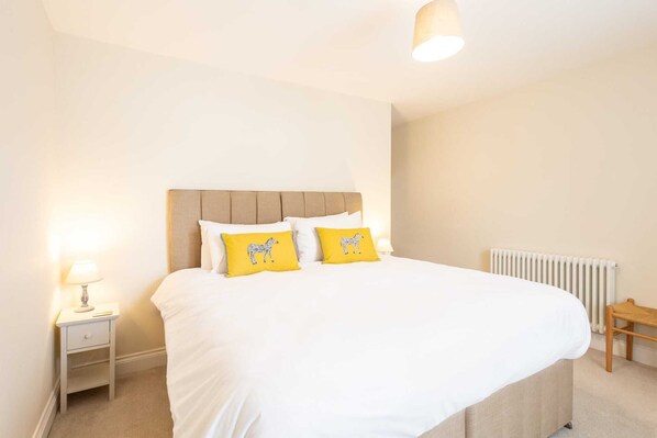 A bedroom with a large bed, a nightstand, a lamp, and a radiator. - Host & Stay | Hotspur Street (Alnwick)