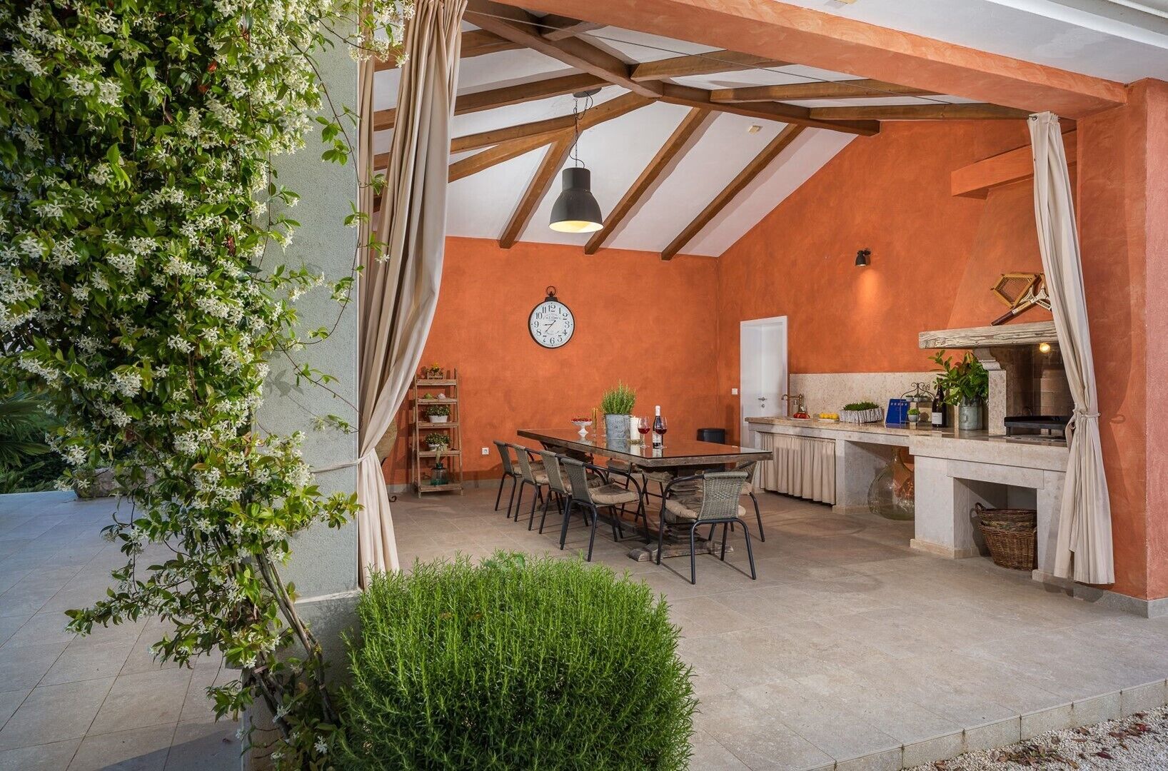 Une cuisine ouverte sur la salle à manger, avec un plafond rustique, une horloge au mur et une table à manger dressée pour quatre personnes.