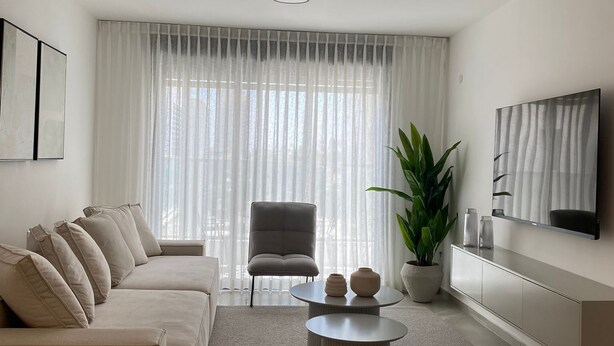 Een moderne woonkamer met een bank, een fauteuil, een salontafel en een televisie aan de muur.