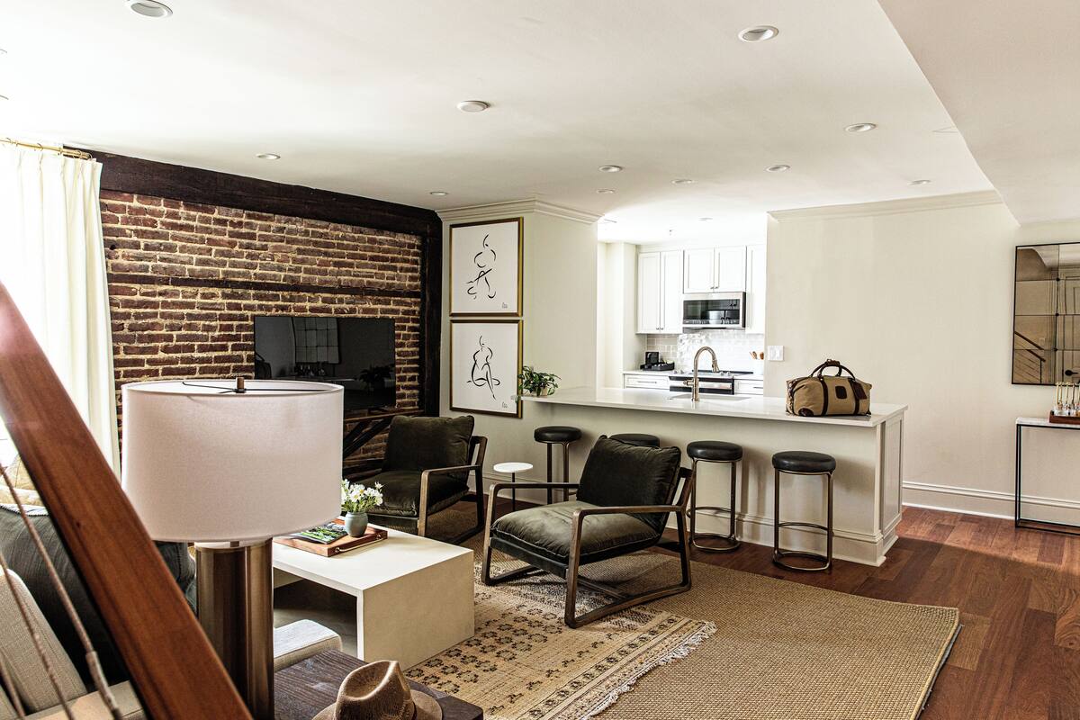 A modern living room with a brick wall, a flat-screen TV, and a dining area with bar stools.