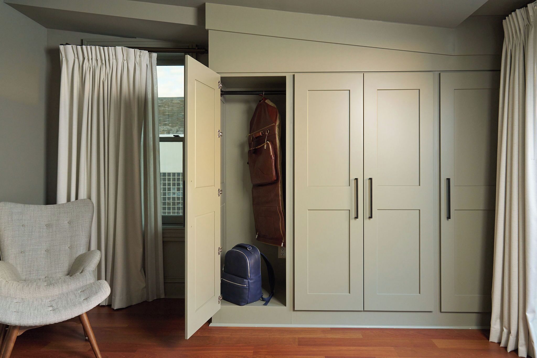 A room with a wardrobe, a chair, and a suitcase.