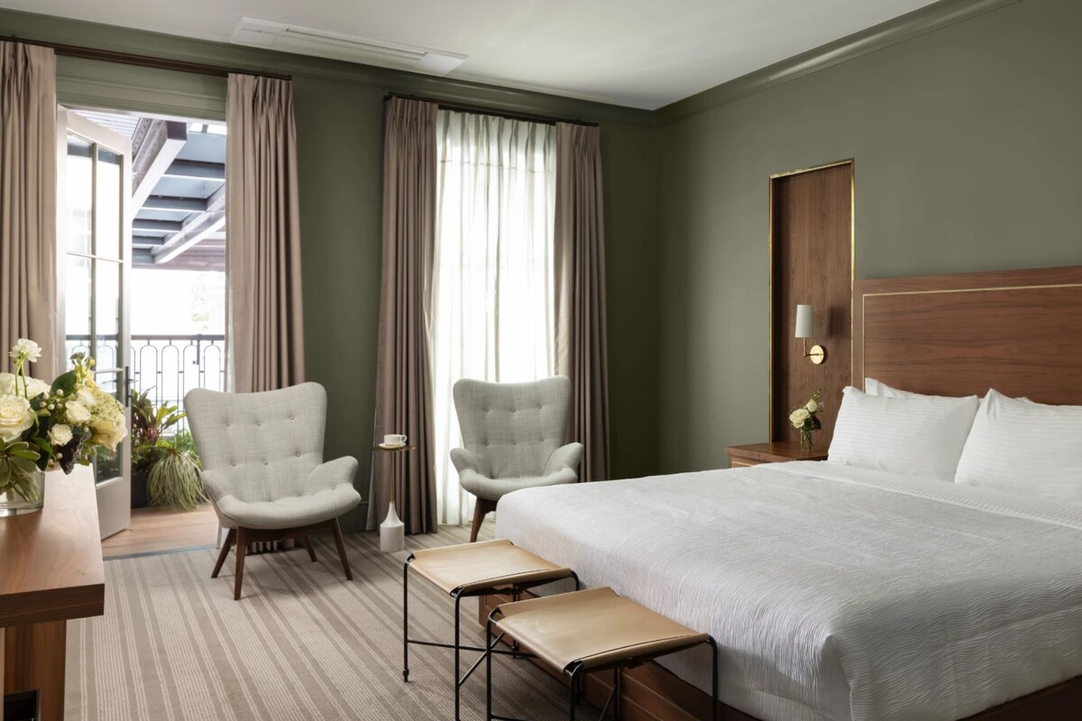 Habitación de hotel con una cama grande, dos sillones, una mesita y una mesita de noche con lámpara.