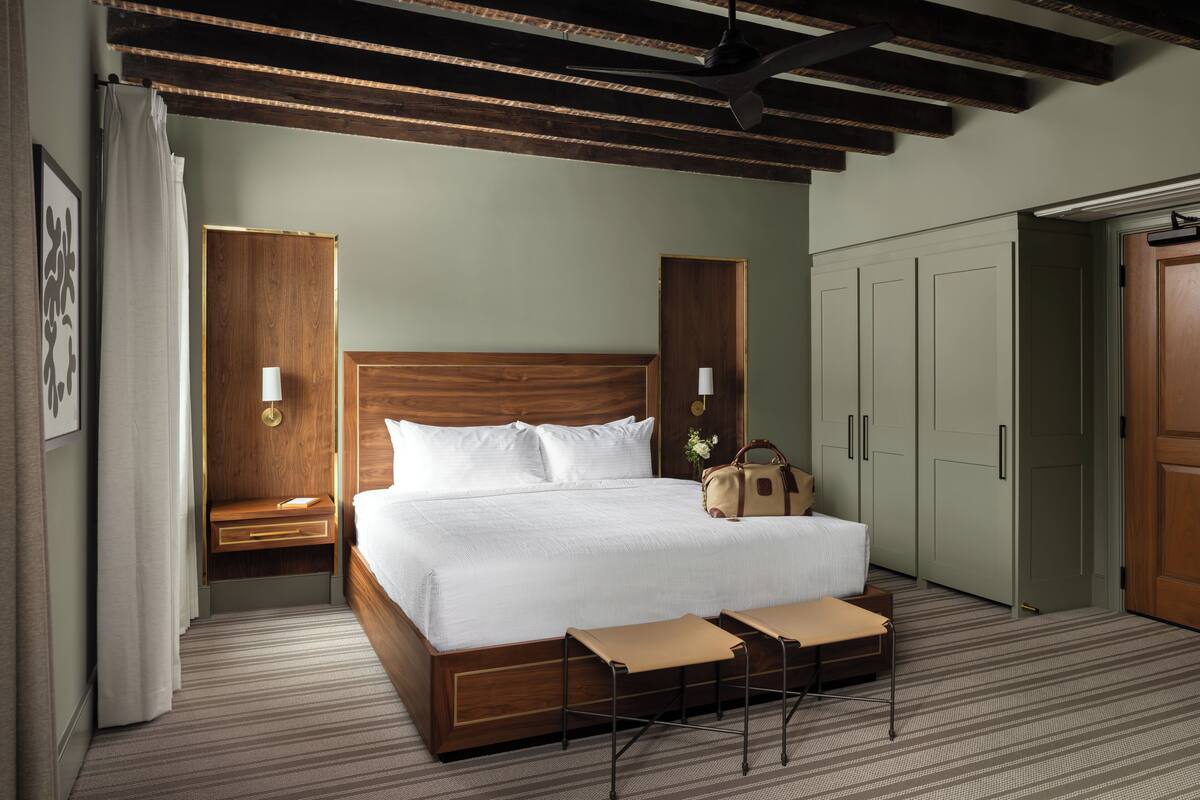 A hotel room with a large bed, wooden headboard, bedside tables, a wardrobe, and a ceiling fan.