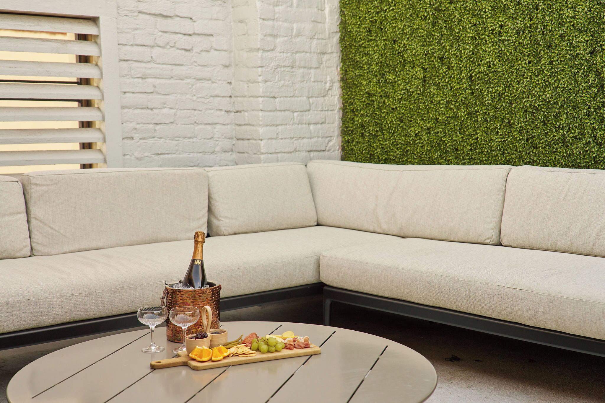 A sectional sofa with a bottle of champagne, glasses, and a charcuterie board on a round table.