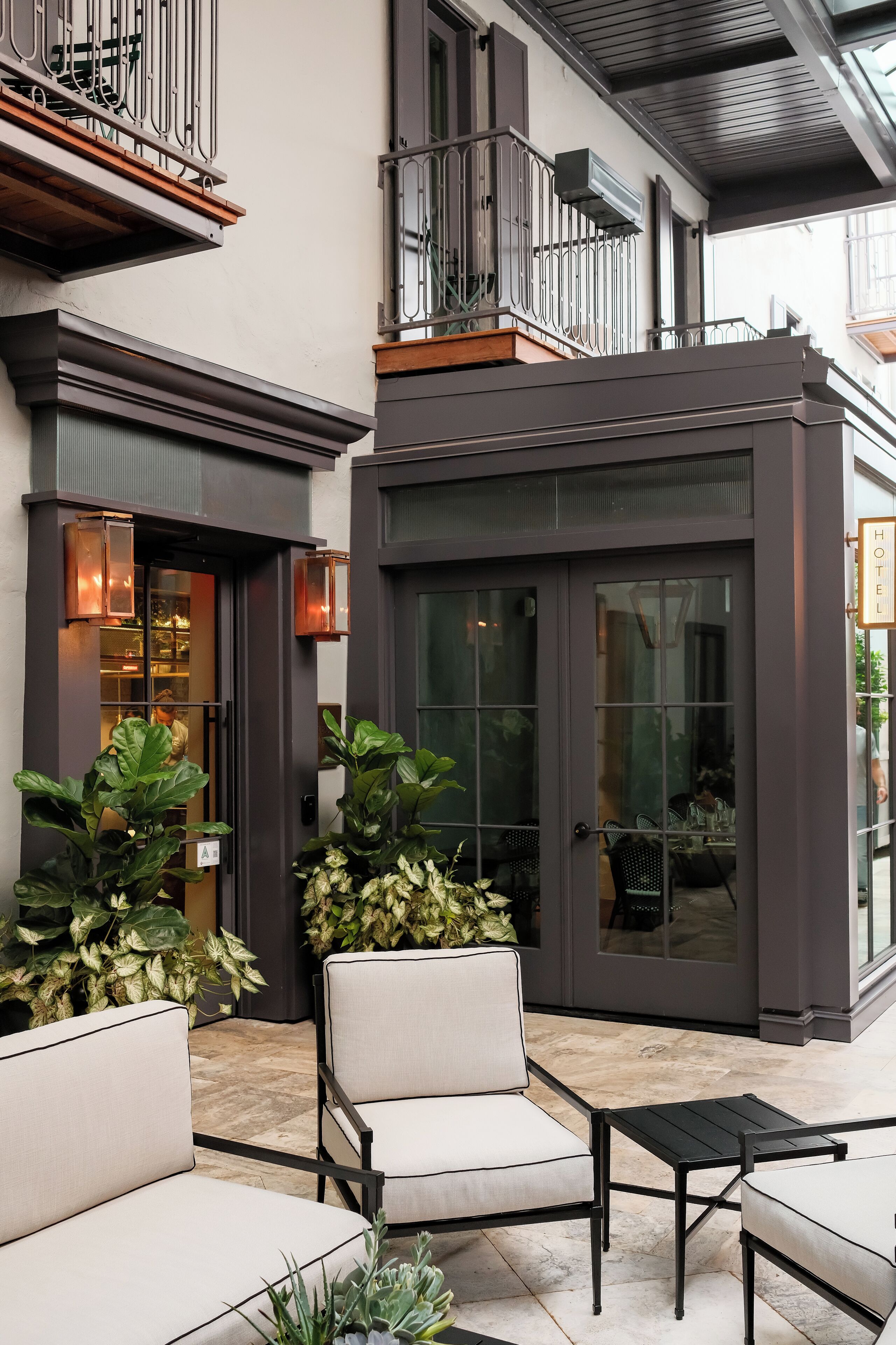 Exterior moderno de un hotel con puerta de vidrio, área de estar al aire libre con sillas y plantas en macetas.