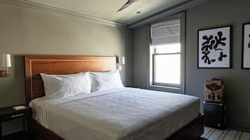 Una cama bien tendida con sábanas blancas, cabecera de madera y mesita de noche con lámpara.