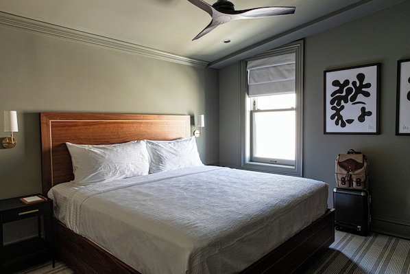A neatly made bed with white linens, a wooden headboard, and a nightstand with a lamp. - Hotel Richemont (Charleston)