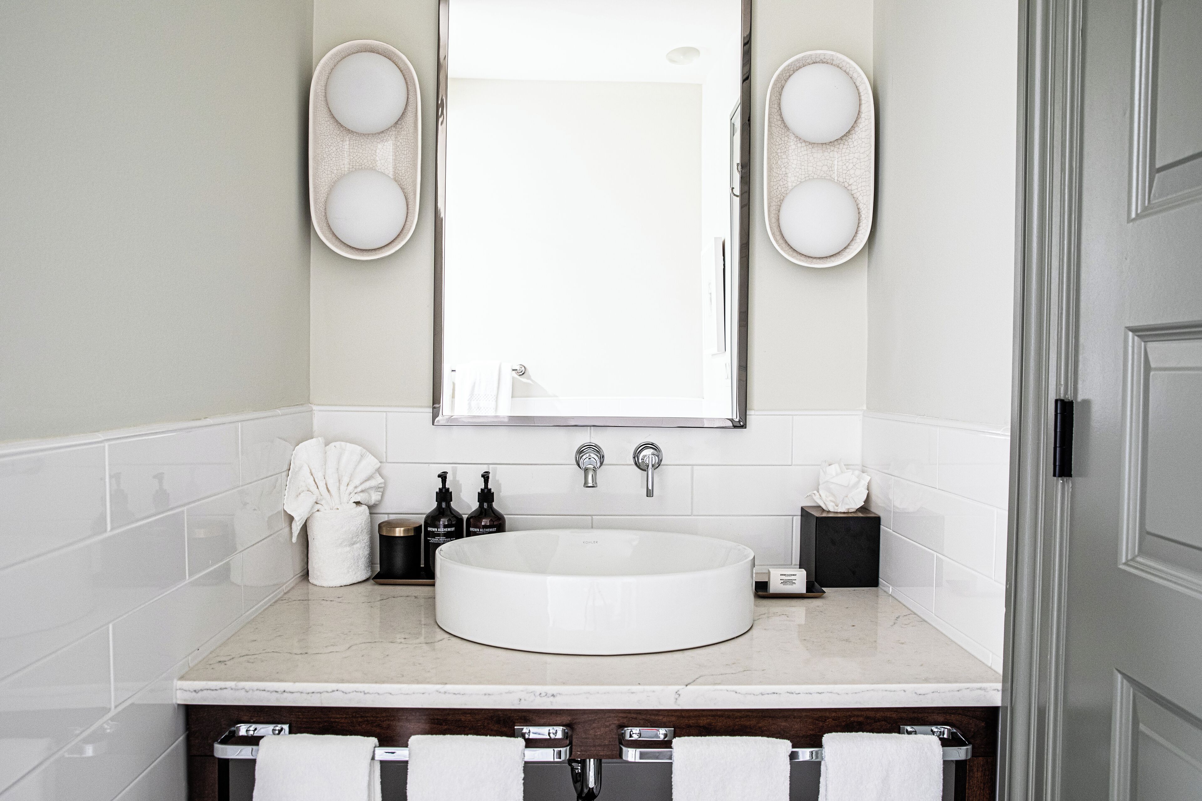 Un baño moderno con un lavabo blanco redondeado, dos grifos, un espejo grande y dos luminarias empotradas.