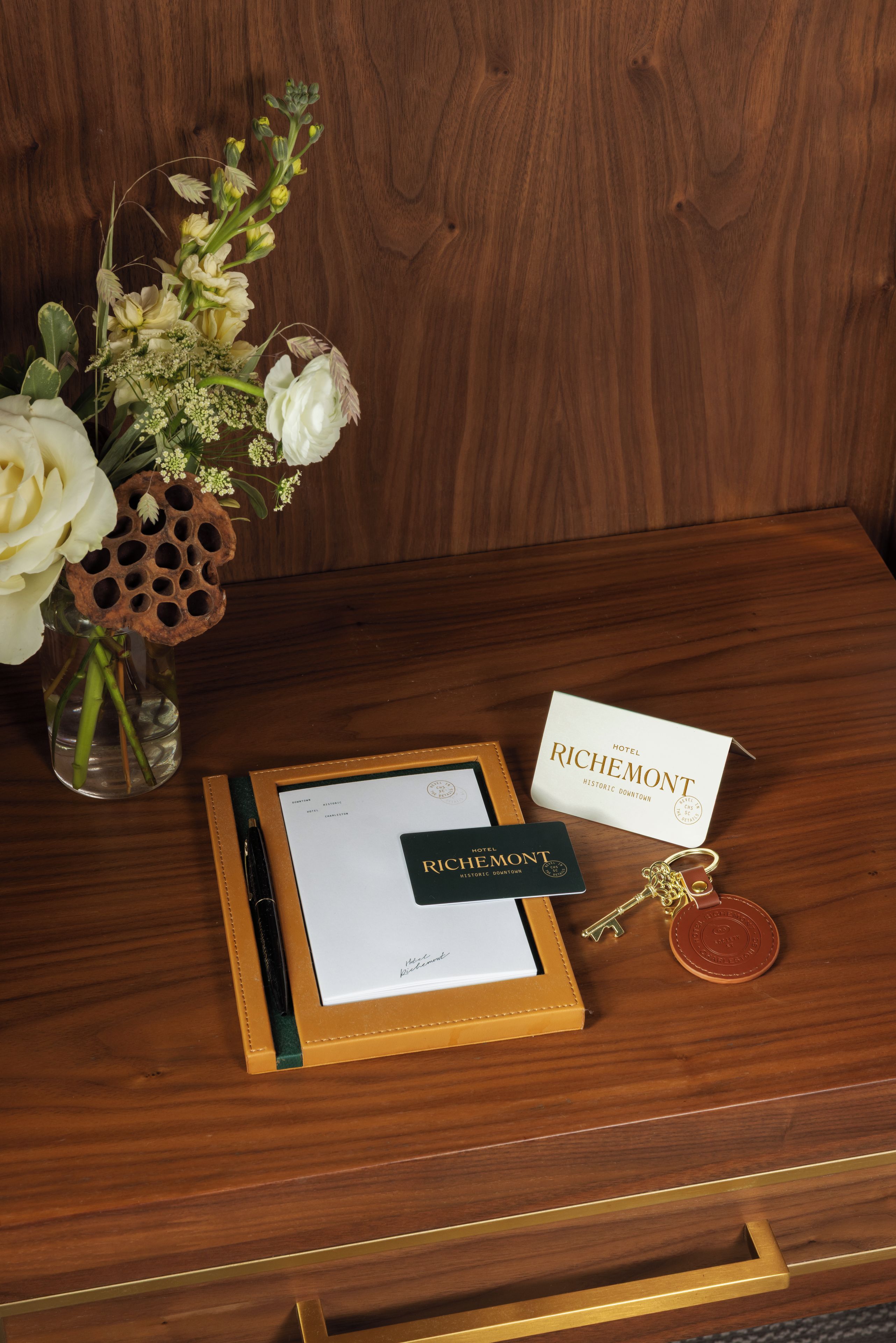 Una mesa de madera con un certificado enmarco, un bolígrafo, un llavero y un florero con flores.