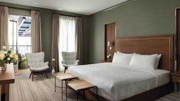 A hotel room with a large bed, two armchairs, a small table, and a view of the outdoors.