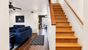Un escalier avec des marches en bois et une rampe, un canapé bleu, un tapis noir et blanc et un ventilateur de plafond.
