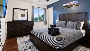 Un dormitorio con cama, ventilador de techo, cómoda, ventana y un cuadro en la pared.
