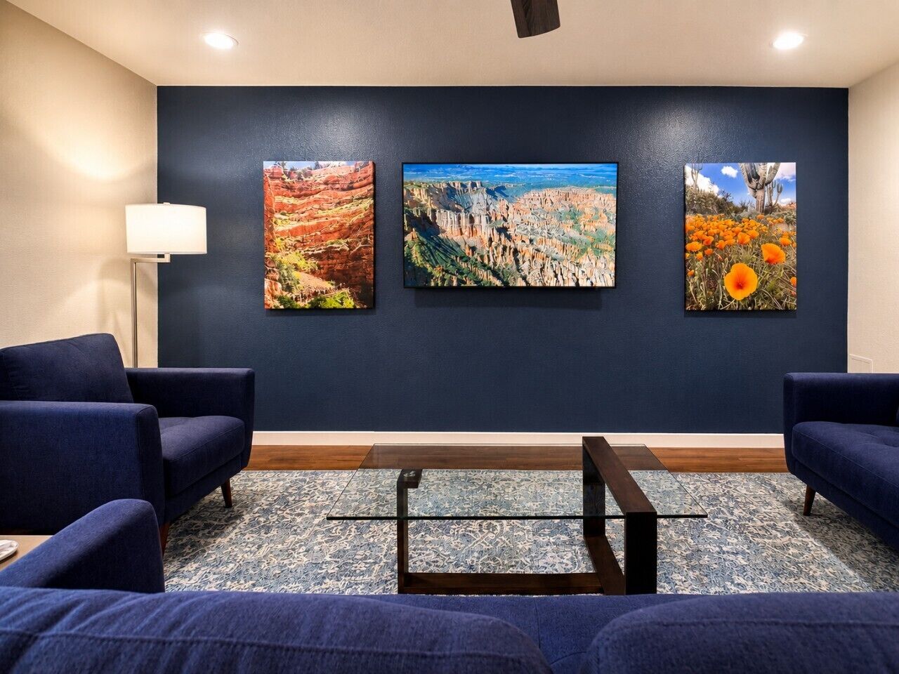 Una habitación con paredes azul oscuro, tres cuadros de paisajes enmarcados, un sofá azul oscuro, una mesita de centro pequeña y una lámpara de pie.