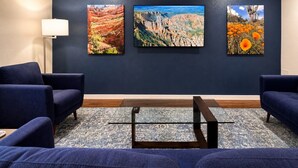 Une pièce aux murs bleu foncé, ornée de trois tableaux représentant des paysages, avec un canapé bleu foncé, une petite table basse et un lampadaire.