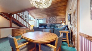A cozy living room with a wooden dining table, comfortable seating, a staircase, and a stone fireplace. - Mammoth Sierra Townhomes #23 4 Bedroom Condo by RedAwning (Mammoth Lakes)