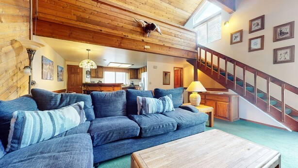 A cozy living room with a blue sofa, wooden ceiling, and a staircase leading to another level. - Mammoth Sierra Townhomes #23 4 Bedroom Condo by RedAwning (Mammoth Lakes)