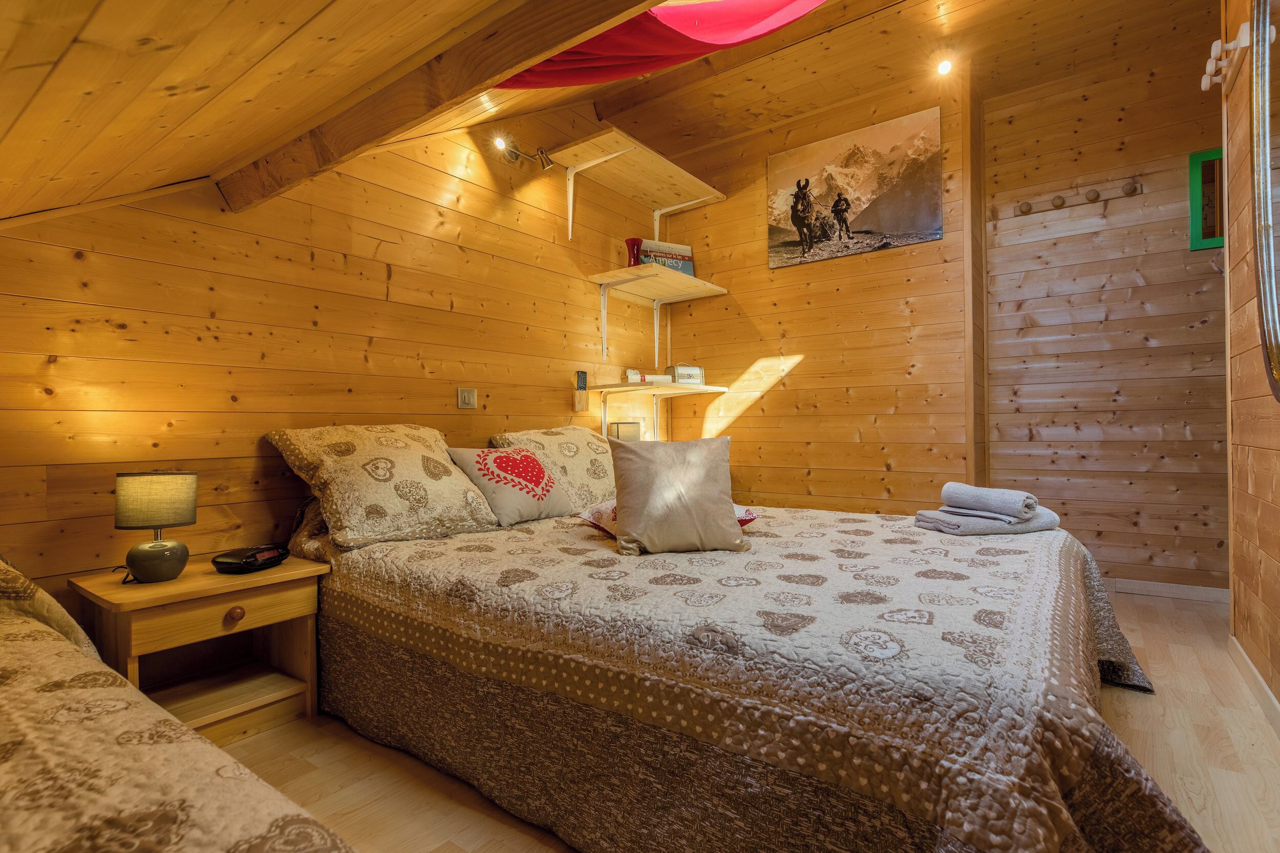 A cozy wooden cabin bedroom with a bed, nightstands, and a shelf with books.