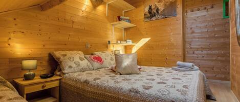 A cozy wooden cabin bedroom with a bed, nightstands, and a shelf with books.