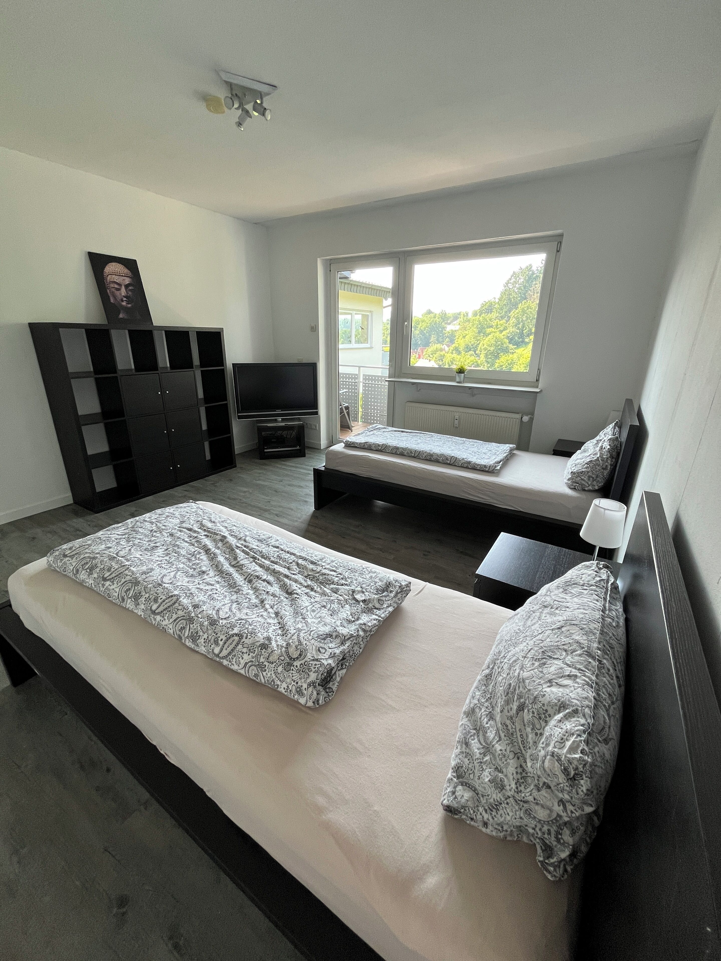 Ein Schlafzimmer mit zwei Betten, einem Fernseher, einem Kleiderschrank und einem Fenster mit Blick auf Grünflächen.