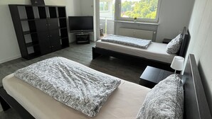 Een slaapkamer met twee bedden, een televisie, een kledingkast en een raam met uitzicht op groen.