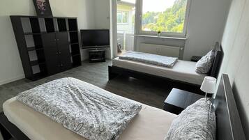 Ein Schlafzimmer mit zwei Betten, einem Fernseher, einem Kleiderschrank und einem Fenster mit Blick auf Grünflächen.