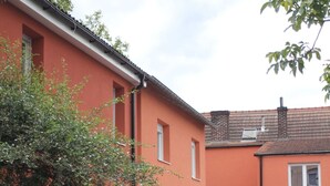 A residential building with a red facade, a gravel driveway, and a small garden area with various plants and outdoor furniture.