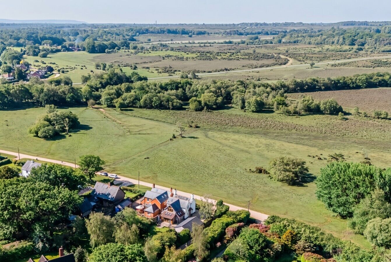 An aerial view of a rural property with a house, green fields, and scattered trees.