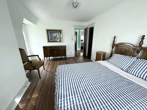 Een slaapkamer met een groot bed, een stoel, een dressoir en een lijst met een afbeelding aan de muur.