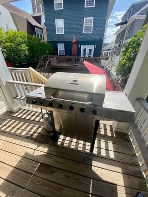 Una parrilla de acero inoxidable sobre una terraza de madera, con una casa azul de fondo.
