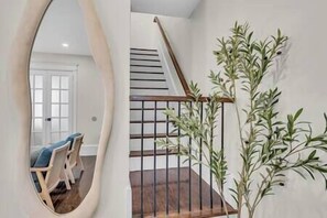 A staircase with wooden steps and a metal railing, a potted plant, and a mirror reflecting a room with a door and a chair.