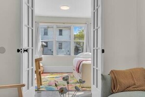 An open door leading to a bedroom with a bed, a window, and a colorful rug.